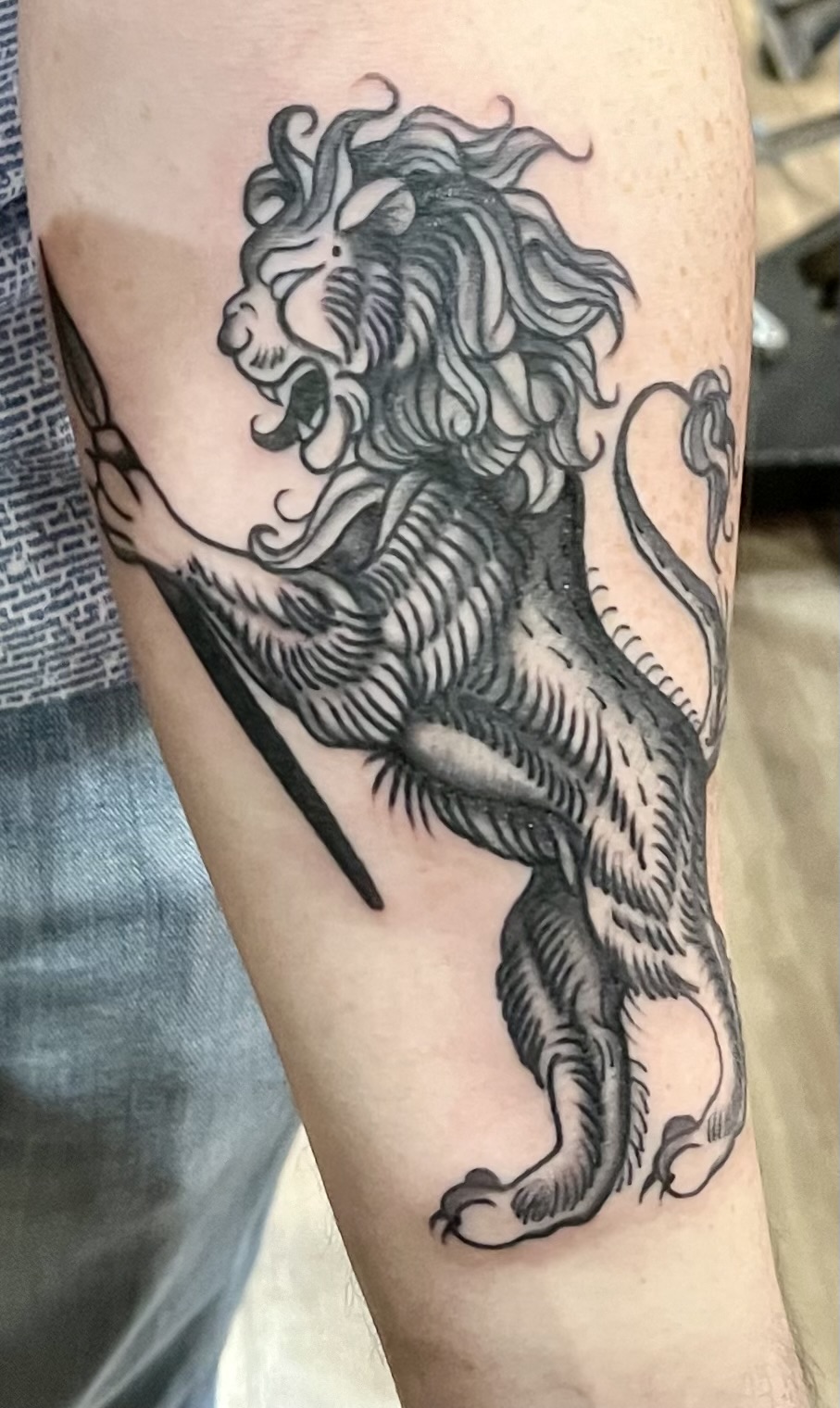 A photo of a forearm with a black and white tattoo. The tattoo is of a heraldic lion holding a fountain pen.